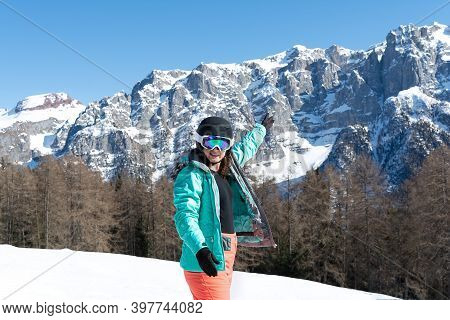 A Woman In A Colorful Ski Suit, Helmet And Sunglasses After Skiing Stands Against The Backdrop Of Mo