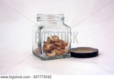 Cashews In The Small Square Shaped Jar With Black Cap On White Background. Cashews Is An Edible Kidn