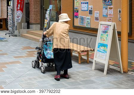 Beppu, Oita, Japan, June 21, 2017: An Elderly Woman With A Stroller Reads An Ad On A Shopping Street