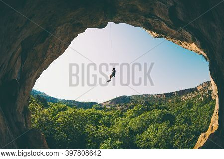 Rock Climber Hanging On A Rope, A Man Climbs A Rock In The Shape Of An Arch, The Man Climbs In The C