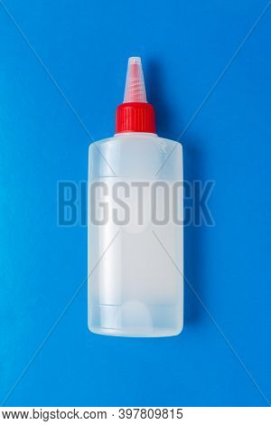 Closed Plastic Bottle Of Stationery Glue For Paper With A Red Cap On A Blue Background