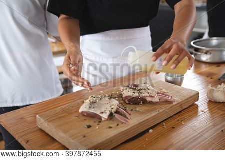 Divserse group of chefs in kitchen. trainee chefs standing at a table, preparing meat with seasonings.