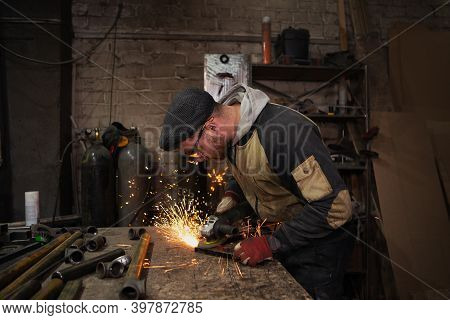 A Male Worker Cuts Metal With A Hand Grinder, Bright Sparks Fly From Under The Saw In All Directions
