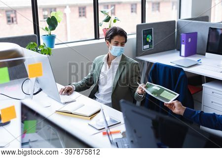 Caucasian businessman wearing face mask using computer in office. social distancing in business office workplace during covid 19 coronavirus pandemic.