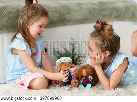 Cheerful Pretty Small Girls Sisters Kids With Long Hair In Same Clorhing Playing With Toys Dolls Tog