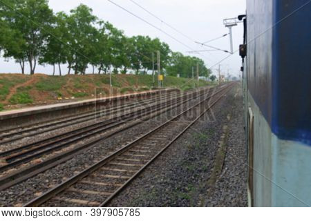 Blurred Image Of Indian Rail Lines With Green Trees In The Side.