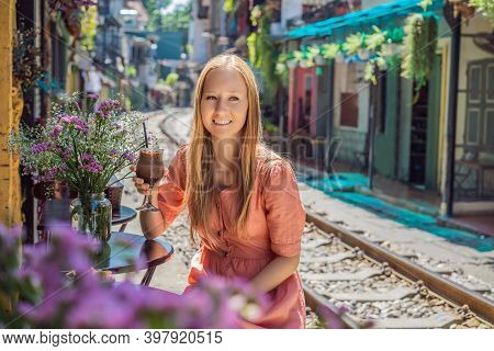 Young Woman Traveler Drinks Coffee Sitting By The Railway Paths Which Go Through Residential Area In