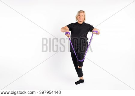 Senior Woman Stretches Elastic Band With Her Leg, On White Empty Space. Healthy, Pandemic Concept.