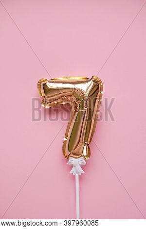 Gold Inflatable Number 7 On A Stick On A Pink Background.