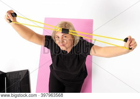 Photo From Above. The Elder Woman With Resistance Band Over Her Head Sitting On The Mat.