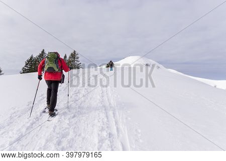 Senior Couple Is Snowshoe Hiking In Alpine Snow Winter Mountains. Allgau, Bavaria, Germany.
