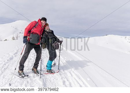 Senior Couple Is Snowshoe Hiking In Alpine Snow Winter Mountains. Allgau, Bavaria, Germany.