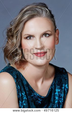Mooie veertig jaar oude vrouw met fashion make-up, krullend kapsel op grijs blauw studio achtergrond.