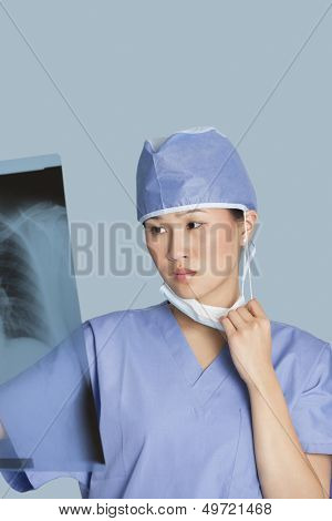 Female surgeon looking at x-ray report over light blue background