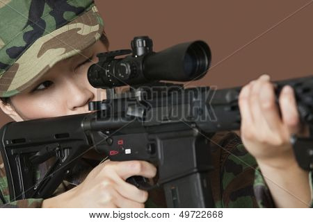 Young female US Marine Corps soldier aiming M4 assault rifle over brown background