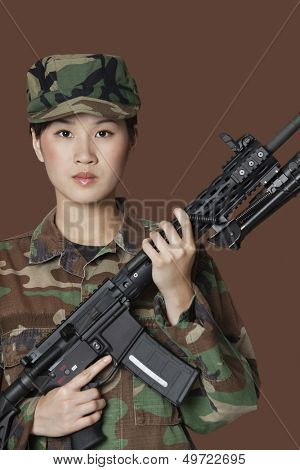 Portrait of beautiful young US Marine Corps soldier with M4 assault rifle over brown background