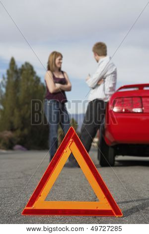 Young couple standing by breakdown car with red warning triangle in foreground