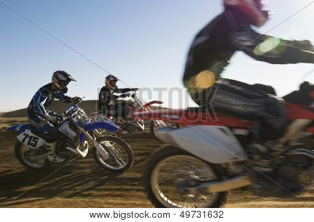 Three motocross racers racing in desert against blue sky