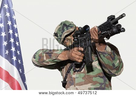 US Marine Corps soldier aiming M4 assault rifle with American flag against gray background