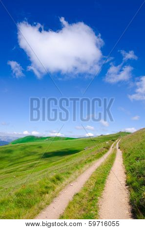 mountain dirt road under a cloud in blue sky - 