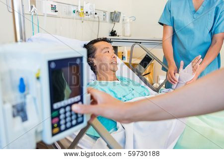 Midsection of nurse putting bandage on patient's hand while coworker operating IV machine in foreground at hospital