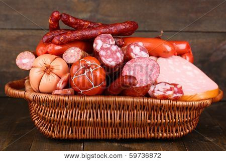 Lot of different sausages in basket on wooden table on wooden background