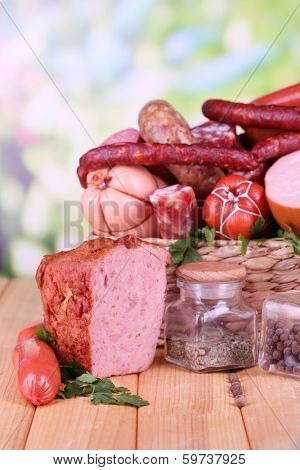 Lot of different sausages in basket on wooden table on natural background