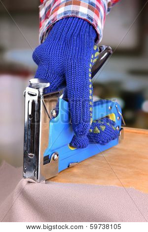 Fastening fabric and wooden box using construction stapler on bright background