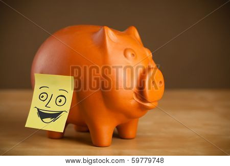 Drawn smiley face on a post-it note sticked on piggy bank