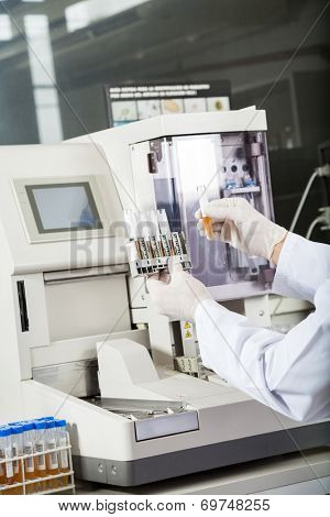 Cropped image of male researcher examining samples by urine analyzer in lab