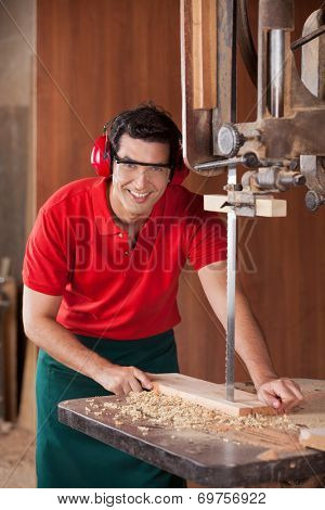 Portrait of confident male carpenter cutting wood with bandsaw in workshop