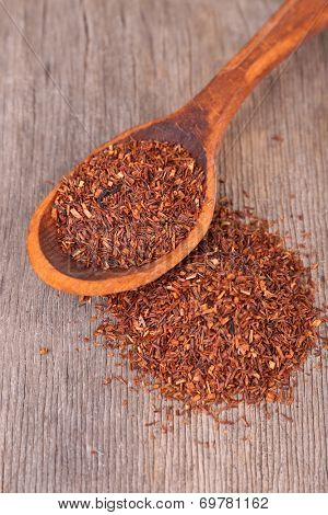 Dried rooibos tea in spoon on wooden table