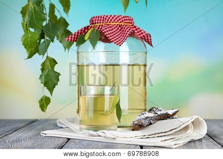 Glass and large flagon of fresh birch sap  on a wooden table on nature background