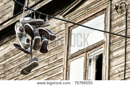 Old sport shoes thrown over black cable with home in the background