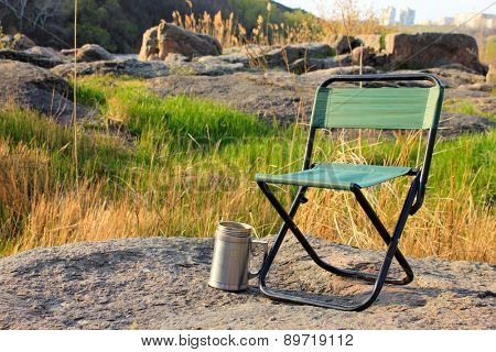 Camp chair and thermos cup on nature background