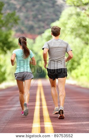 Runners running and jogging for health and fitness. People on fitness run on road in nature. Couple, woman and man training outside for fitness and healthy life. Full body length rear view of back.
