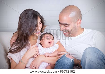 Portrait of happy cheerful family sitting on the couch at home, young parents enjoying time spent with their adorable newborn daughter