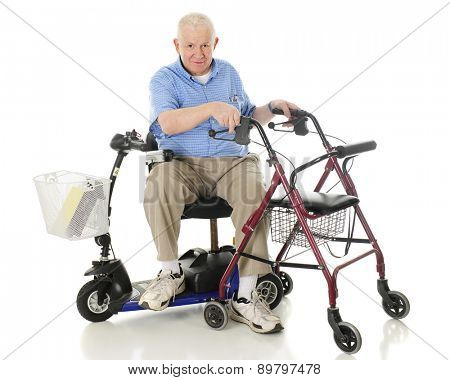 A senior man sitting sideways on his power scooter while holding onto the handles of his wheeling walker.  On a white background.