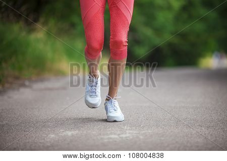 Cropped view of woman athlete running on pathway in park.