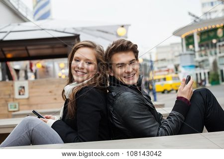 Couple Holding Mobile Phones While Sitting Back To Back
