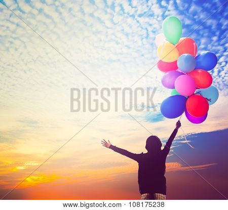 girl holding bunch of air balloons at sunset sky