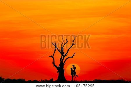 Silhouette of couple in love with big sunset and dead tree.