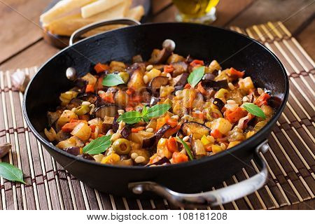 Italian Caponata with frying pan on a wooden background.