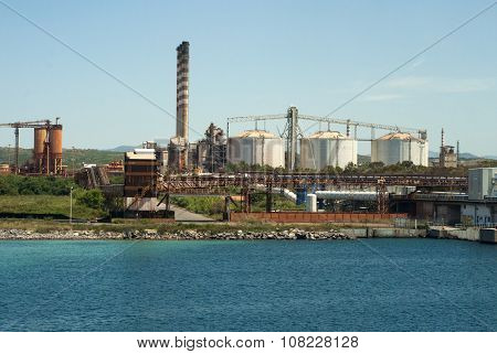 Petrochemical Factory With Tanks And Pipelines Surrounded By Nature And Blue Sea