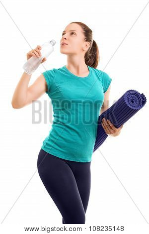 Portrait of a beautiful young girl holding an exercise mat and drinking water from a bottle, isolated on white background.