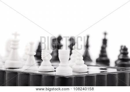 A close up shot of a black and white chess table, with white figures in focus and black figures blurred, isolated on white background.