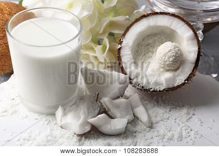 Candies in coconut flakes and fresh coconut on color wooden background