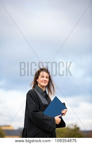 Pretty, young woman celebrating joyfully her graduation - spreading wide her arms, holding her diploma, savouring her success (color toned image; shallow DOF)
