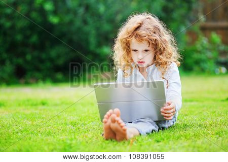 Little Girl Sitting On Grass And Playing Tablet Pc, Toning Photo.