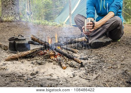 Girl Sitting While Camping Near The Fire Heated And Drink Hot Tea